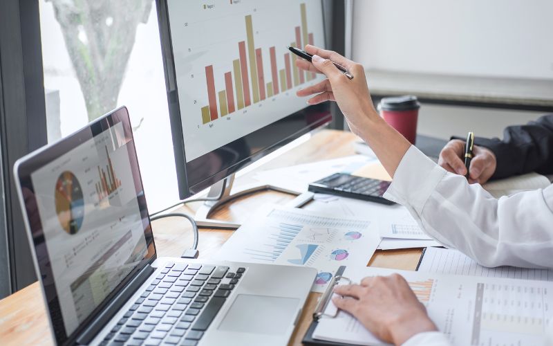 Someone looking at reports on two different screens, pointing a pen at one screen