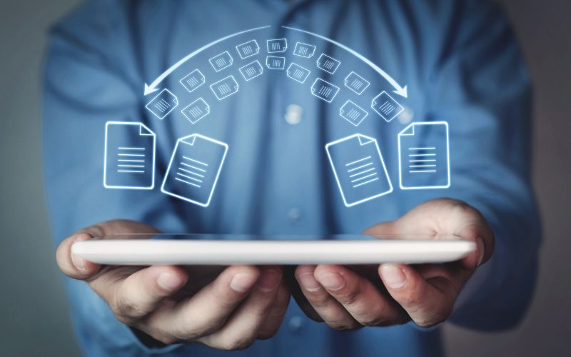 An image of a man holding an ipad with a graphic of files being transferred over the top